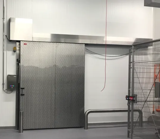 La imagen muestra una puerta corredera automática de acero inoxidable, diseñada para entornos industriales que requieren altos estándares de higiene y eficiencia.