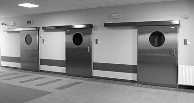Pasillo de hospital con paredes blancas y dos puertas de acero, ejemplo de áreas que deben considerarse en el mantenimiento preventivo hospitalario para seguridad y durabilidad.