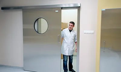 Médico abre una puerta hospitalaria corrediza con ventana integrada, fabricada según la NOM infraestructura y equipamiento de hospitales para optimizar el flujo y la visibilidad en áreas médicas.